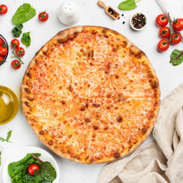 Cheese pizza from above surrounded by tomatoes, oil and basil