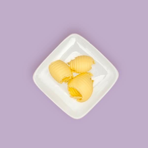 Three curls of butter made from yellow fat blends on a white plate