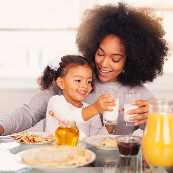 Mother and daughter at breakfast table each with a glass of milk 