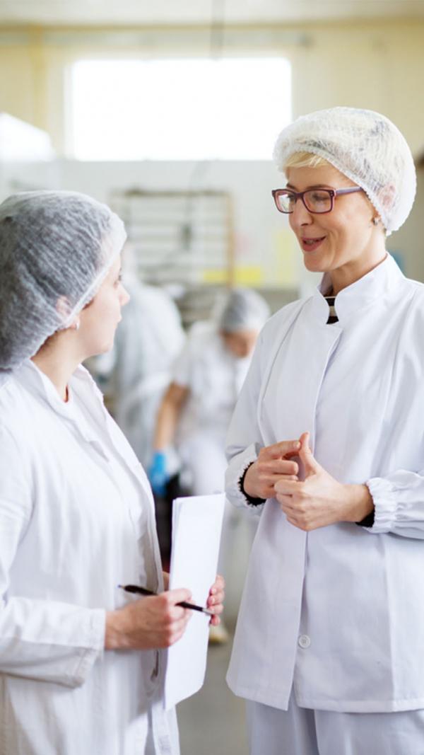 Two women in a  factory discussing ingredients 